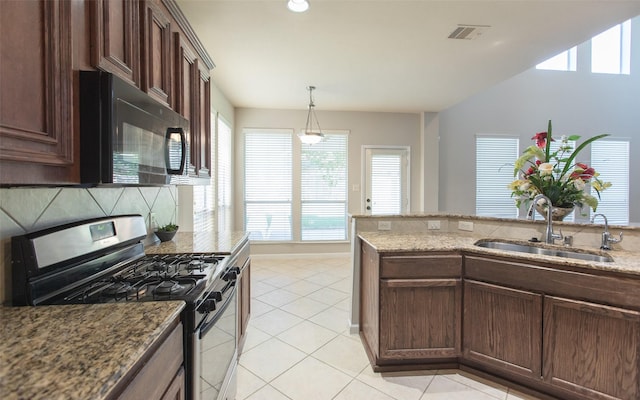 kitchen featuring stainless steel gas stove, a sink, black microwave, light tile patterned floors, and light stone counters
