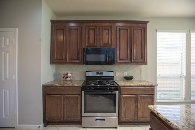kitchen with black microwave, stainless steel range with gas cooktop, backsplash, light tile patterned flooring, and light stone counters