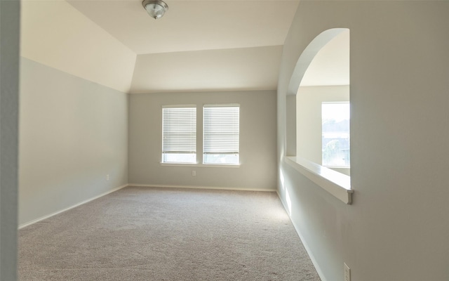 carpeted spare room featuring baseboards and arched walkways