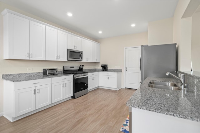 kitchen featuring stainless steel appliances, a sink, light wood-style flooring, white cabinets, and light stone countertops