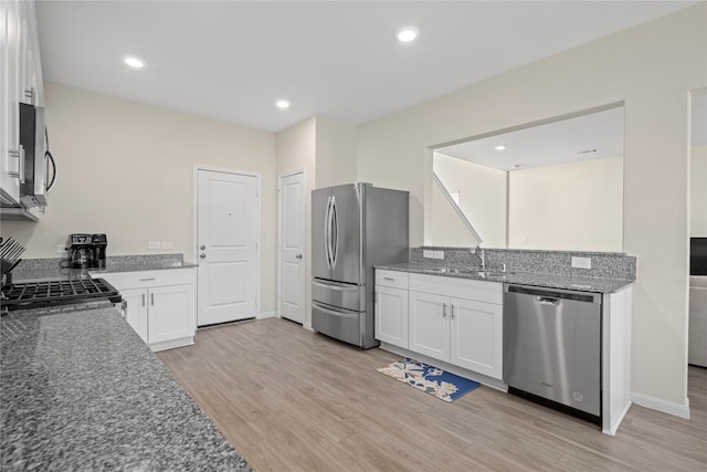 kitchen featuring appliances with stainless steel finishes, a sink, white cabinets, light wood-type flooring, and dark stone countertops