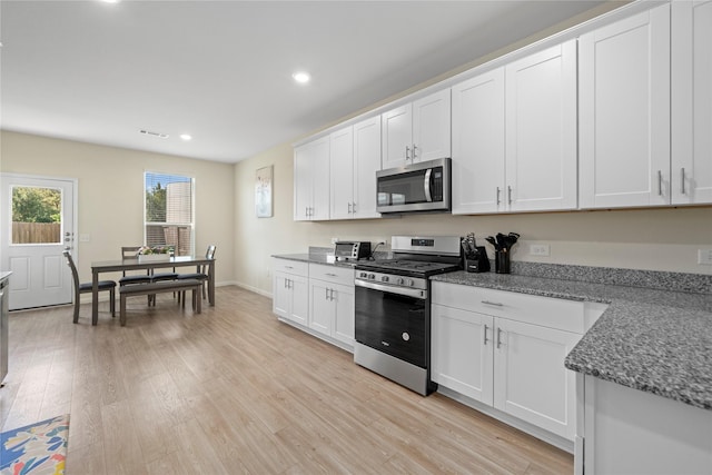 kitchen with appliances with stainless steel finishes, white cabinets, light wood-style flooring, recessed lighting, and dark stone counters