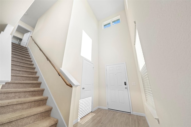 entrance foyer with a towering ceiling, stairway, light wood-type flooring, and baseboards