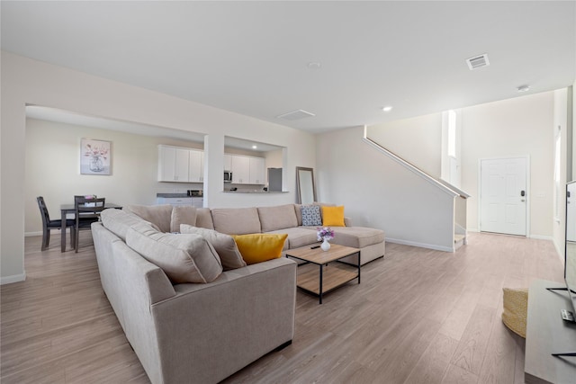 living area with light wood-style flooring, stairs, and baseboards