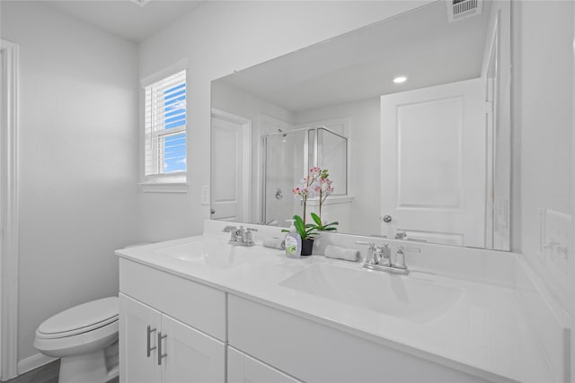 bathroom featuring a shower stall, double vanity, and toilet