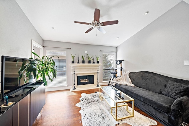 living room featuring vaulted ceiling, ceiling fan, wood finished floors, a fireplace with raised hearth, and recessed lighting