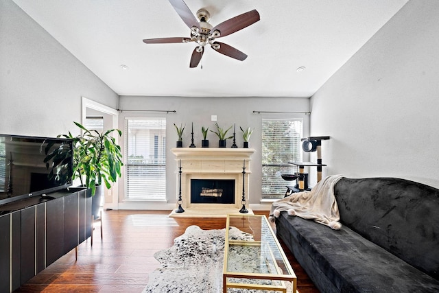 living area with a fireplace with raised hearth, wood finished floors, a ceiling fan, and baseboards