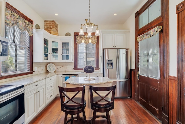 kitchen with appliances with stainless steel finishes, a chandelier, plenty of natural light, glass insert cabinets, and wainscoting