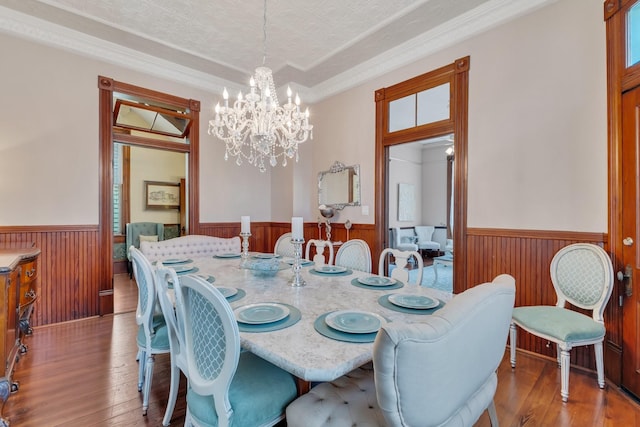 dining area featuring a wainscoted wall, wood-type flooring, wooden walls, a chandelier, and ornamental molding