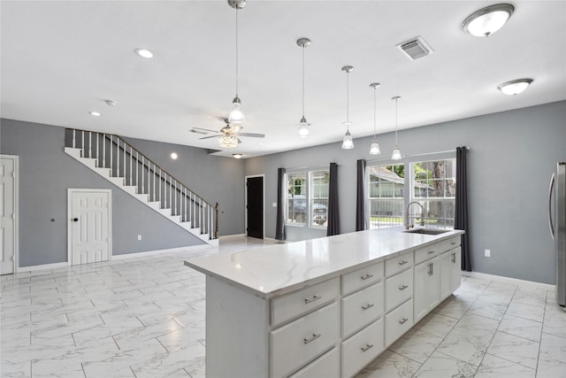 kitchen with light marble finish flooring, white cabinetry, a sink, freestanding refrigerator, and baseboards
