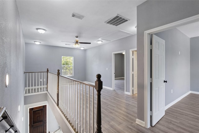 hallway with an upstairs landing, attic access, wood finished floors, and baseboards