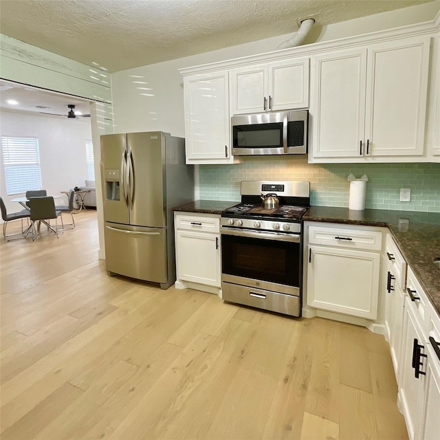 kitchen with appliances with stainless steel finishes, light wood finished floors, white cabinets, decorative backsplash, and a textured ceiling