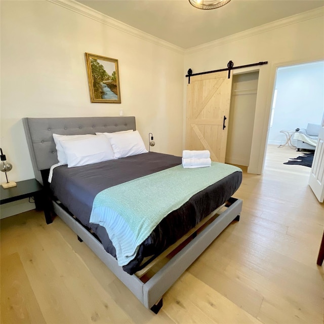 bedroom featuring crown molding, a barn door, and light wood-style floors