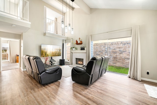 living area with high vaulted ceiling, wood finished floors, a lit fireplace, and baseboards