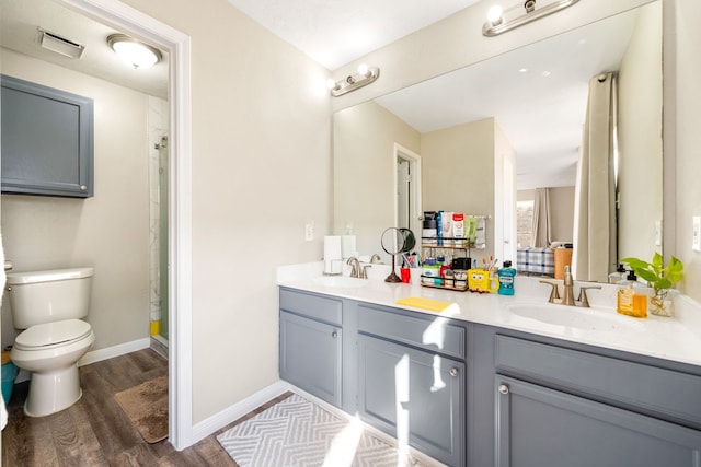 bathroom with toilet, wood finished floors, double vanity, a shower, and baseboards