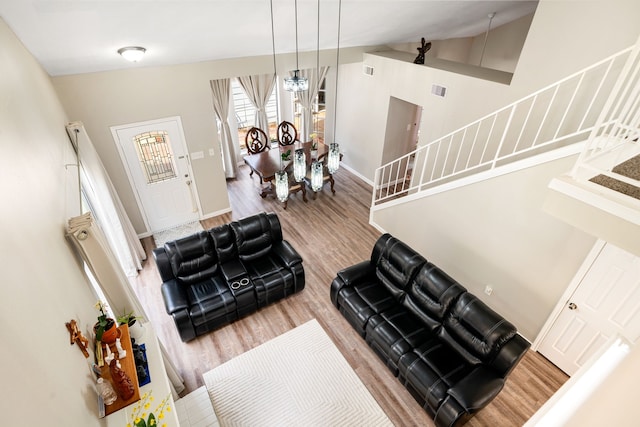 living area featuring stairway, wood finished floors, vaulted ceiling, baseboards, and a chandelier