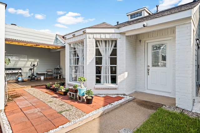 property entrance with brick siding, a deck, and roof with shingles