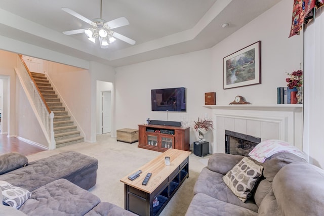 515 Deer Hollow Dr, Sugar Land, TX 77479 - carpeted living room featuring ceiling fan, stairs, a tiled fireplace, a tray ceiling, and baseboards