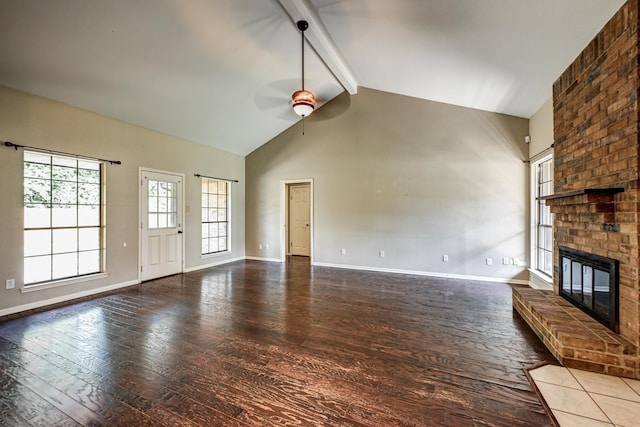 unfurnished living room featuring hardwood / wood-style floors, ceiling fan, beam ceiling, a brick fireplace, and baseboards