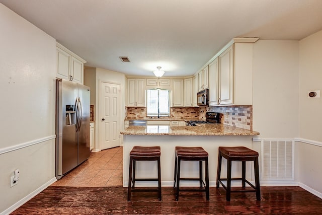 kitchen featuring appliances with stainless steel finishes, a peninsula, cream cabinetry, and decorative backsplash