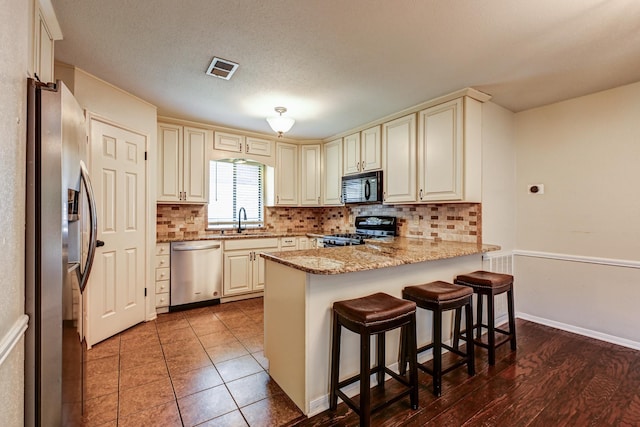 kitchen featuring stainless steel appliances, a sink, cream cabinets, and a peninsula