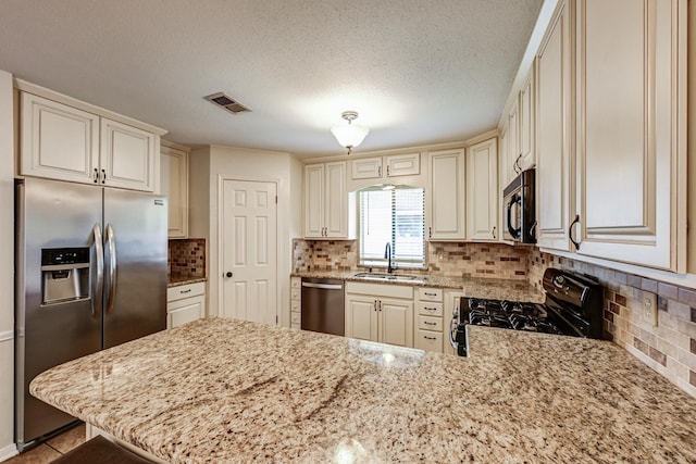 kitchen with black appliances, a sink, a peninsula, cream cabinetry, and backsplash