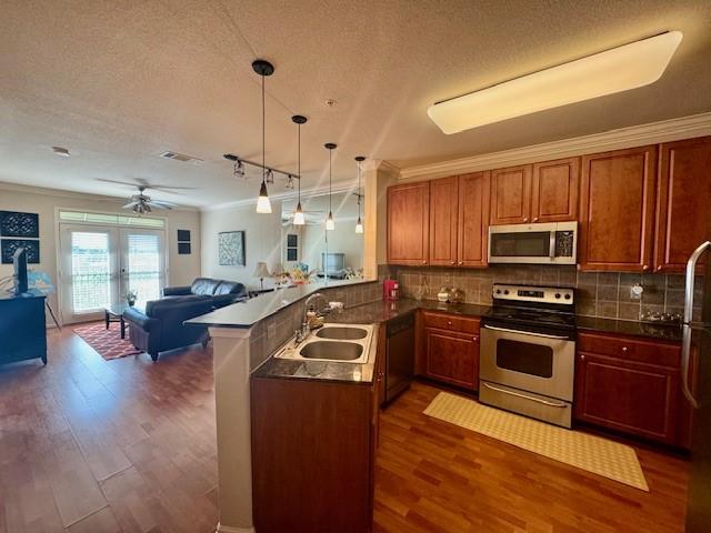 kitchen featuring stainless steel appliances, a sink, open floor plan, dark wood-type flooring, and dark countertops
