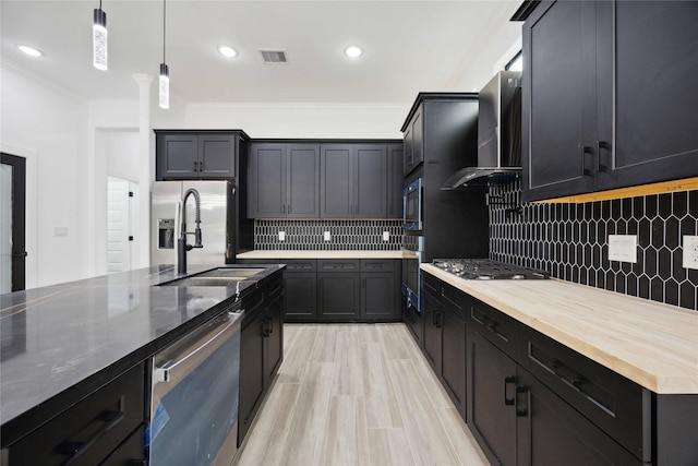 kitchen featuring stainless steel appliances, a sink, wall chimney range hood, ornamental molding, and decorative backsplash
