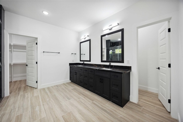 full bath with wood finished floors, double vanity, baseboards, and a walk in closet