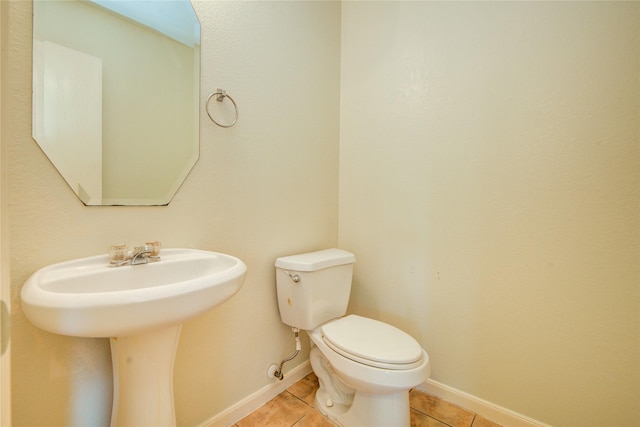 half bath featuring tile patterned flooring, toilet, baseboards, and a sink