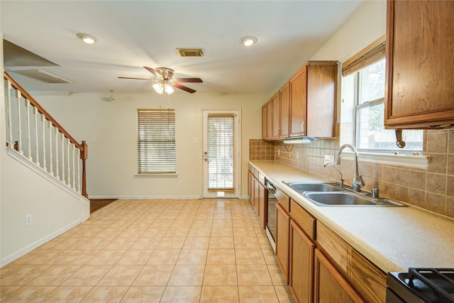 kitchen with a sink, backsplash, ceiling fan, light countertops, and brown cabinetry