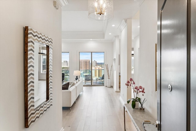 hallway featuring a tray ceiling, light wood-style floors, crown molding, baseboards, and recessed lighting