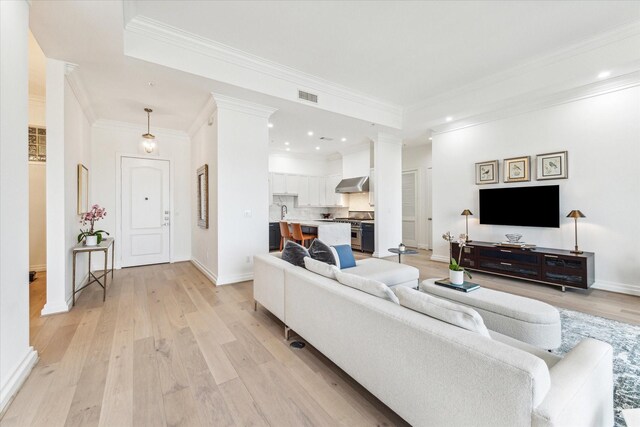 living area with light wood-style floors, baseboards, crown molding, ornate columns, and recessed lighting