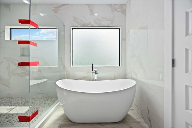 bathroom featuring a soaking tub, a marble finish shower, tile walls, and marble finish floors