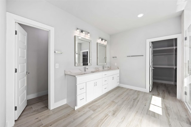 bathroom with wood finished floors, double vanity, baseboards, and a walk in closet