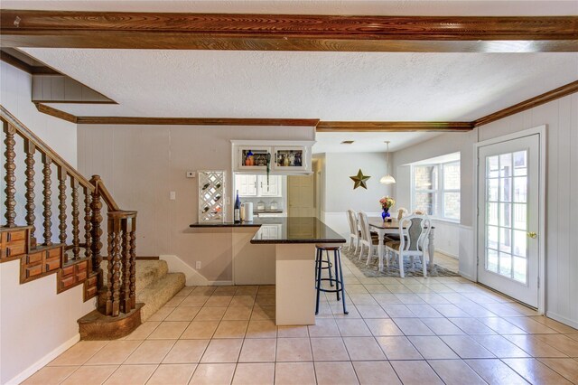 1223 Green Briar Dr, Huntsville, TX 77340 - kitchen featuring a breakfast bar area, dark countertops, light tile patterned floors, a peninsula, and beam ceiling