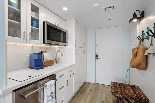 5220 Seawall Blvd Unit 1231, Galveston, TX 77551 - kitchen featuring stainless steel appliances, a sink, light wood-style floors, glass insert cabinets, and light countertops