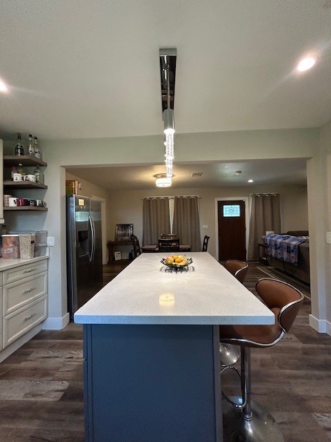 kitchen with stainless steel refrigerator with ice dispenser, light countertops, a kitchen bar, and dark wood-style flooring