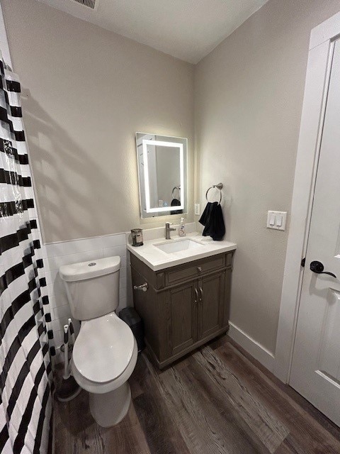 bathroom featuring wood finished floors, toilet, tile walls, vanity, and a wainscoted wall