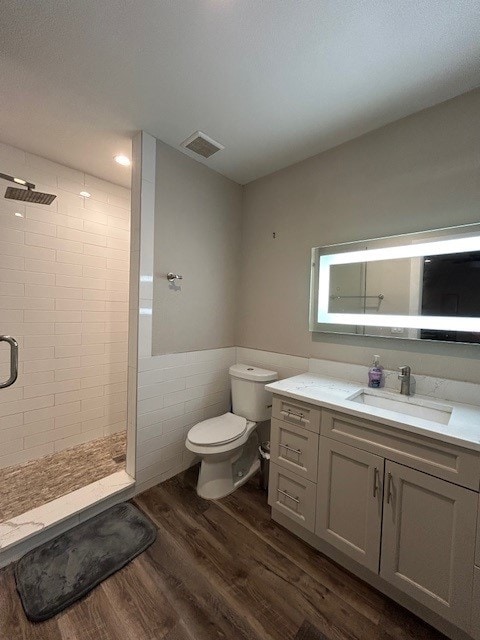 bathroom with a stall shower, wood finished floors, toilet, a wainscoted wall, and vanity