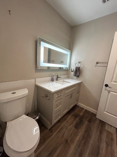 half bathroom with wood finished floors, toilet, vanity, and wainscoting
