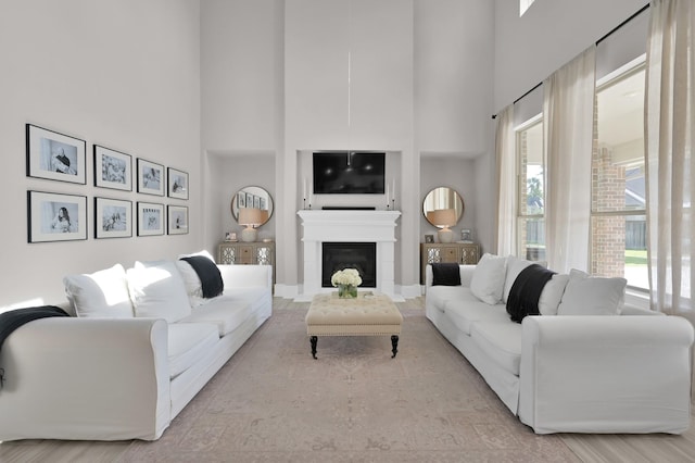 living area with wood finished floors, a towering ceiling, baseboards, and a glass covered fireplace