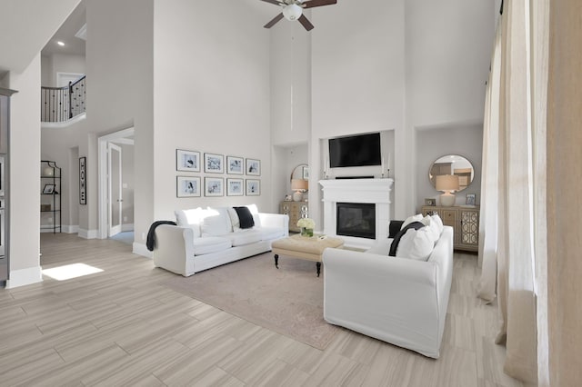 living room with a towering ceiling, ceiling fan, baseboards, light wood finished floors, and a glass covered fireplace