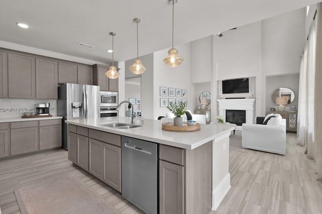 kitchen with appliances with stainless steel finishes, a sink, gray cabinetry, light countertops, and a towering ceiling