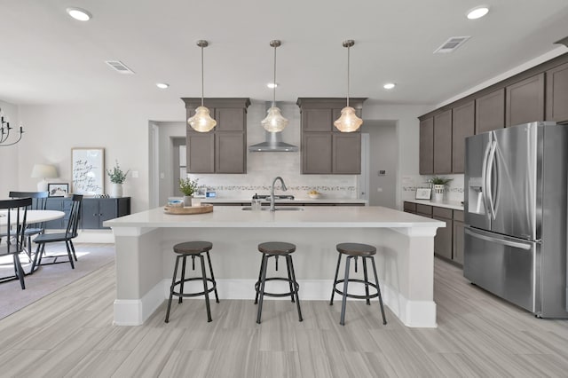 kitchen with stainless steel fridge, wall chimney exhaust hood, a sink, tasteful backsplash, and light countertops