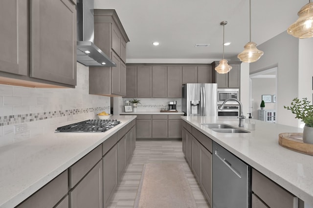 kitchen featuring wall chimney exhaust hood, appliances with stainless steel finishes, a sink, hanging light fixtures, and tasteful backsplash