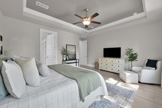 bedroom featuring a raised ceiling, light wood finished floors, crown molding, and ceiling fan