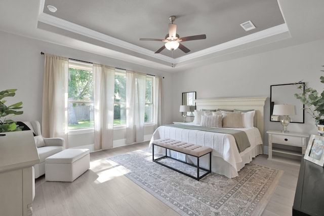 bedroom with a tray ceiling, crown molding, light wood finished floors, and a ceiling fan
