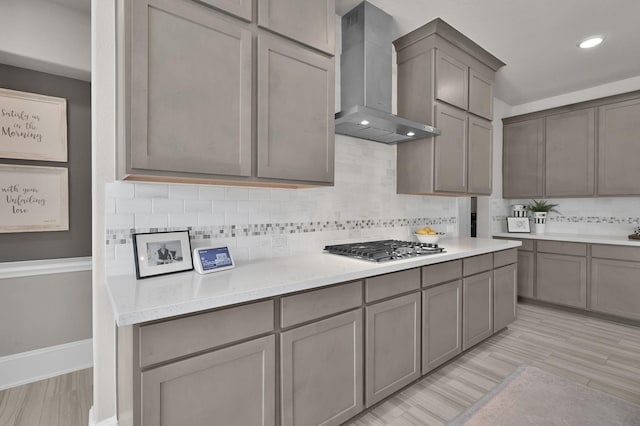 kitchen with wall chimney exhaust hood, stainless steel gas cooktop, backsplash, light countertops, and gray cabinets