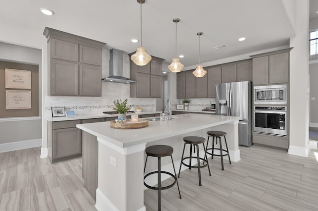kitchen with appliances with stainless steel finishes, wall chimney range hood, a sink, decorative backsplash, and light countertops